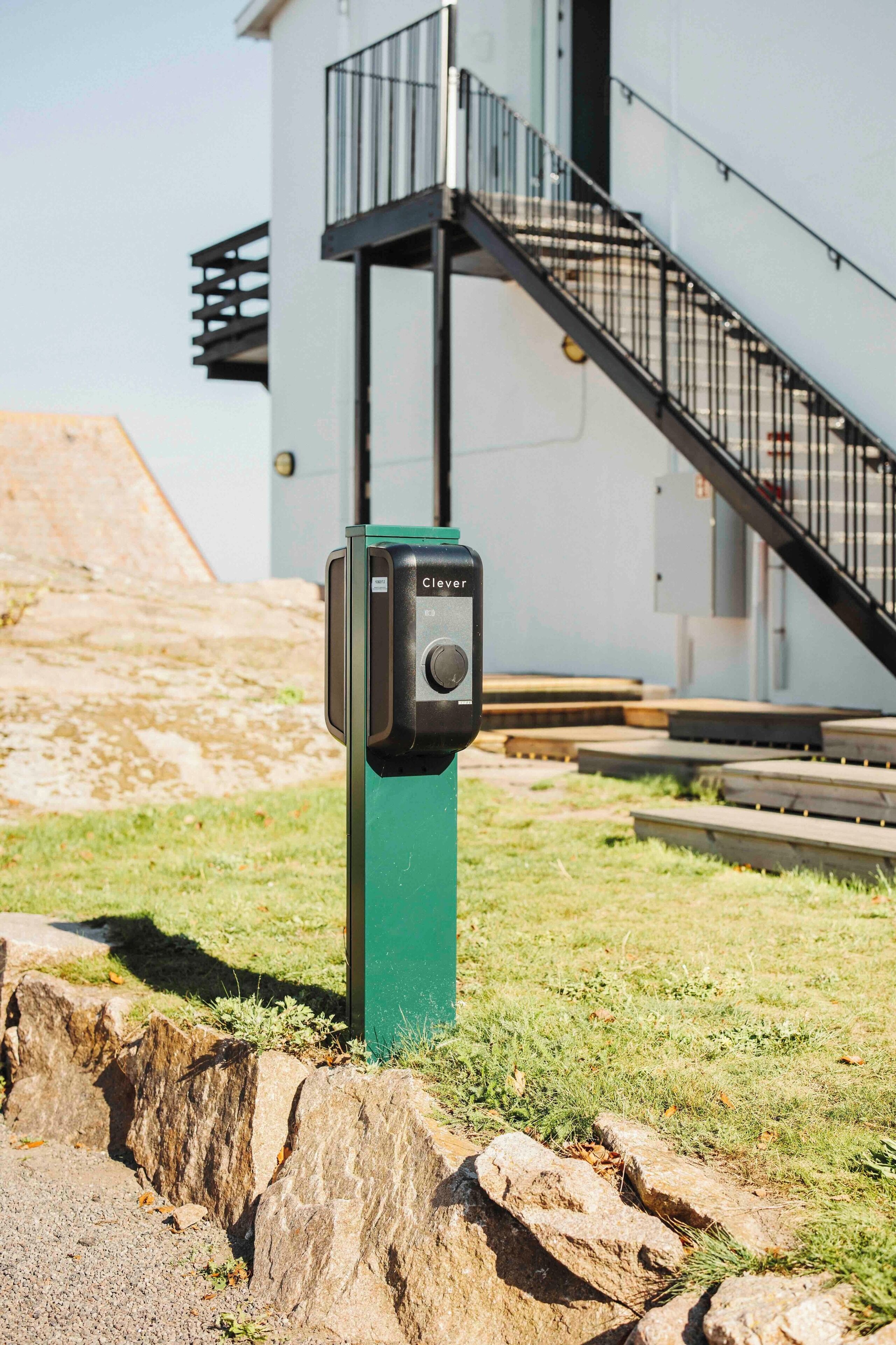 A green utility box with a control panel labeled "Clever" in front of a building with a staircase and a metal railing.