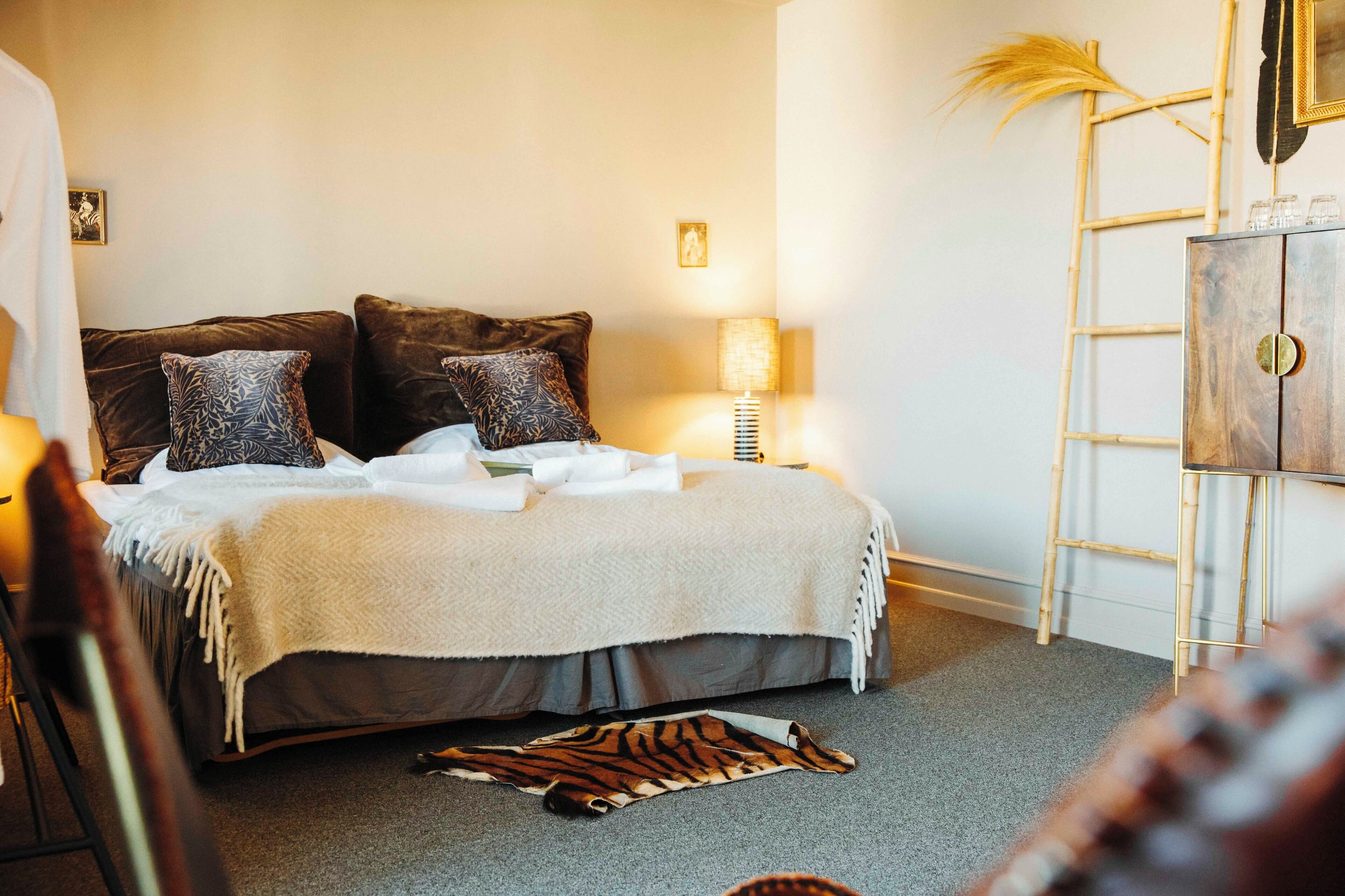 A bedroom with a bed, pillows, a bedside lamp, a wooden wardrobe, and a decorative plant.