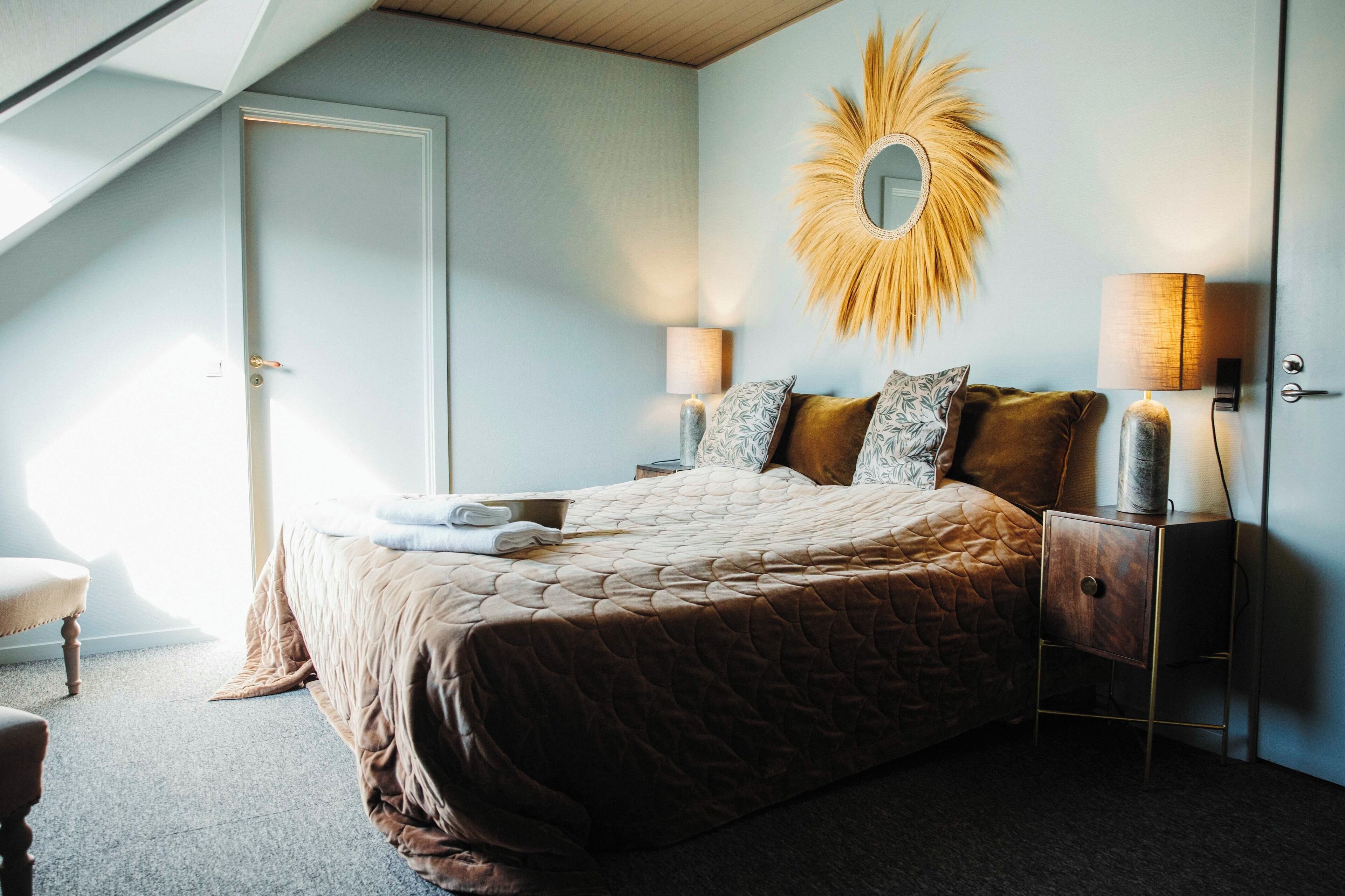 A bedroom with a bed, a nightstand, a lamp, a mirror, and a door.