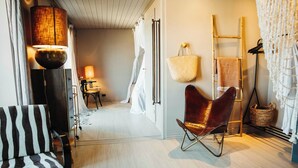 Une pièce comprenant une chaise à rayures, un fauteuil en cuir, une lampe, une échelle et un panier en osier.