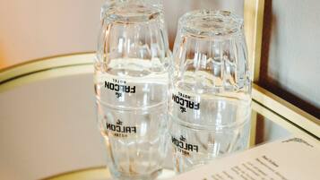 Deux bouteilles en verre transparent portant l’étiquette « FALCON HOTEL », posées sur une surface réfléchissante, avec une partie d’un menu ou d’un dépliant visible.