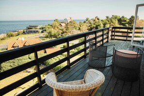 A wooden deck with wicker chairs and a table, overlooking a coastal area with houses and greenery. - The Falcon Hotel (Allinge)