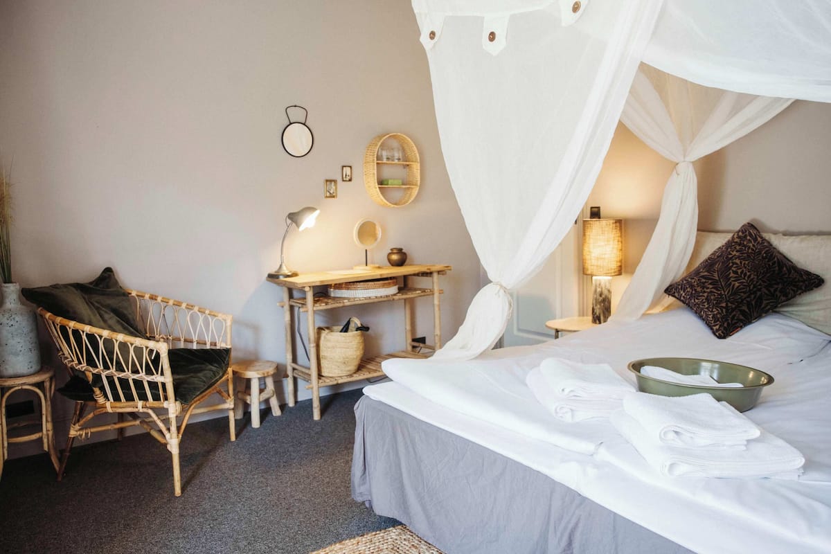 Un dormitorio ordenado con cama, una silla, un escritorio y una mesita de noche.