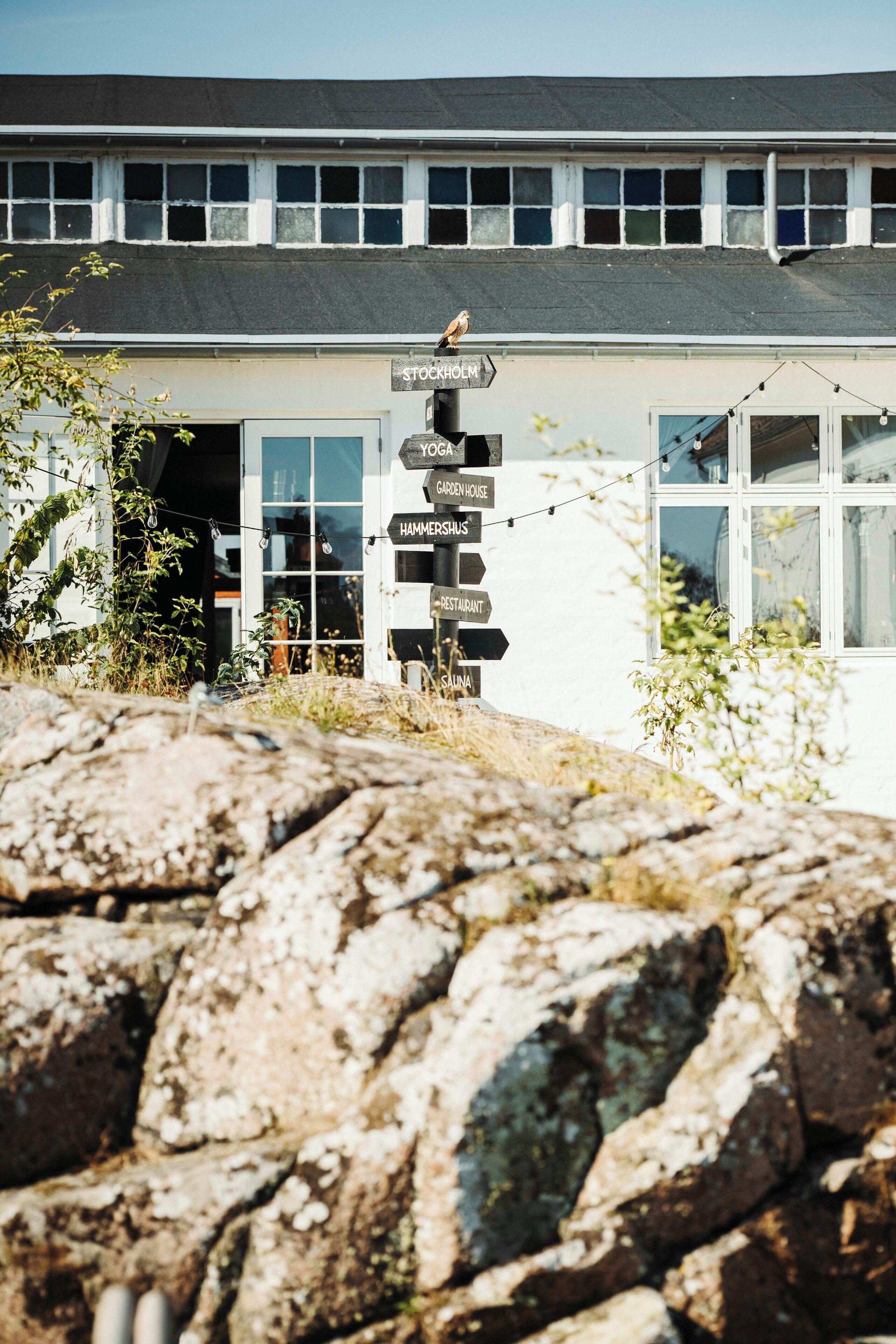 A building with a signpost indicating directions to various establishments including a stockroom, tavern, greenhouse, hammershals, restaurant, and sauna.
