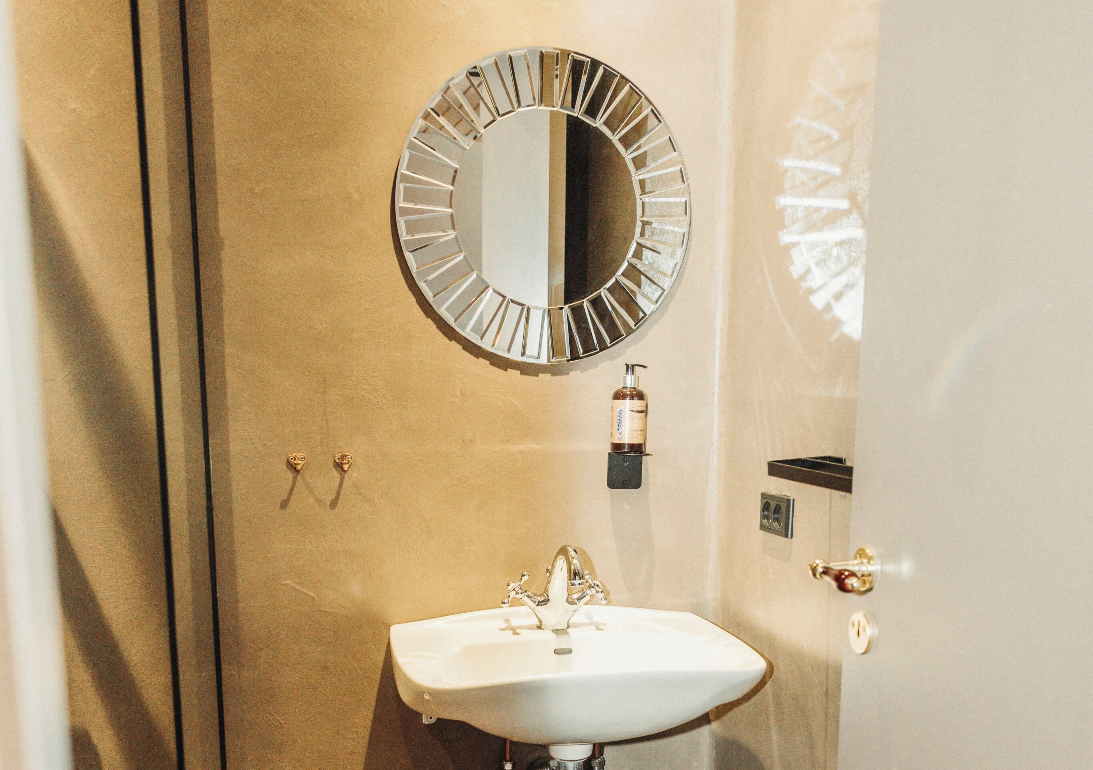 A bathroom with a round mirror, a white sink, and a towel rack.