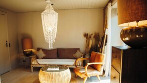 Un salon chaleureux avec un canapé, deux fauteuils, une table basse ronde, un lustre et une lampe.