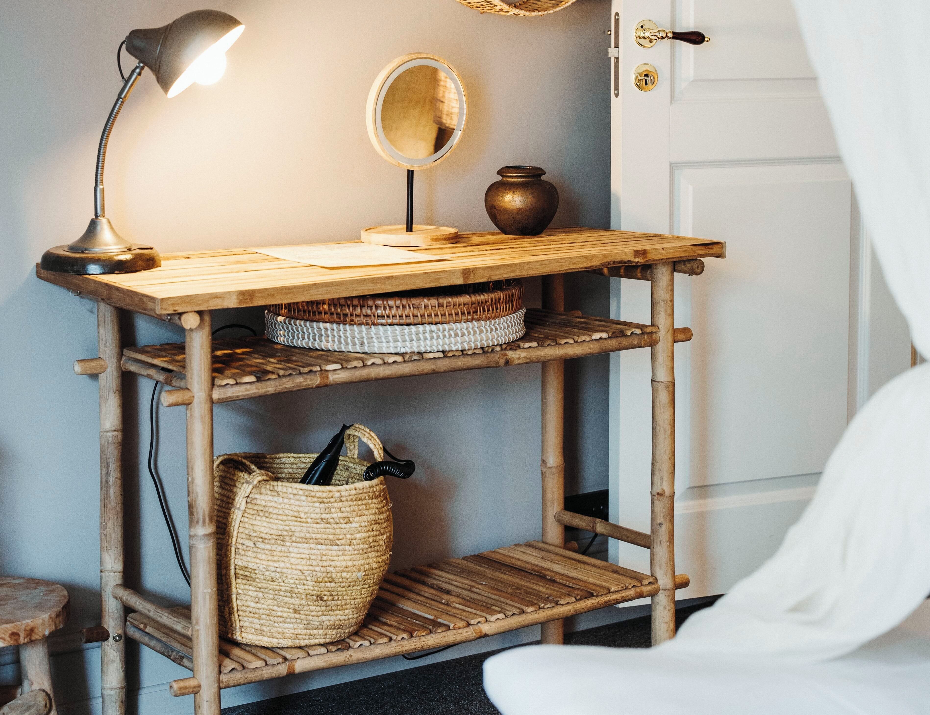 A wooden console table with a lamp, mirror, and woven baskets.