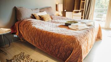 A large bed with a brown quilt, pillows, and a bowl of towels.