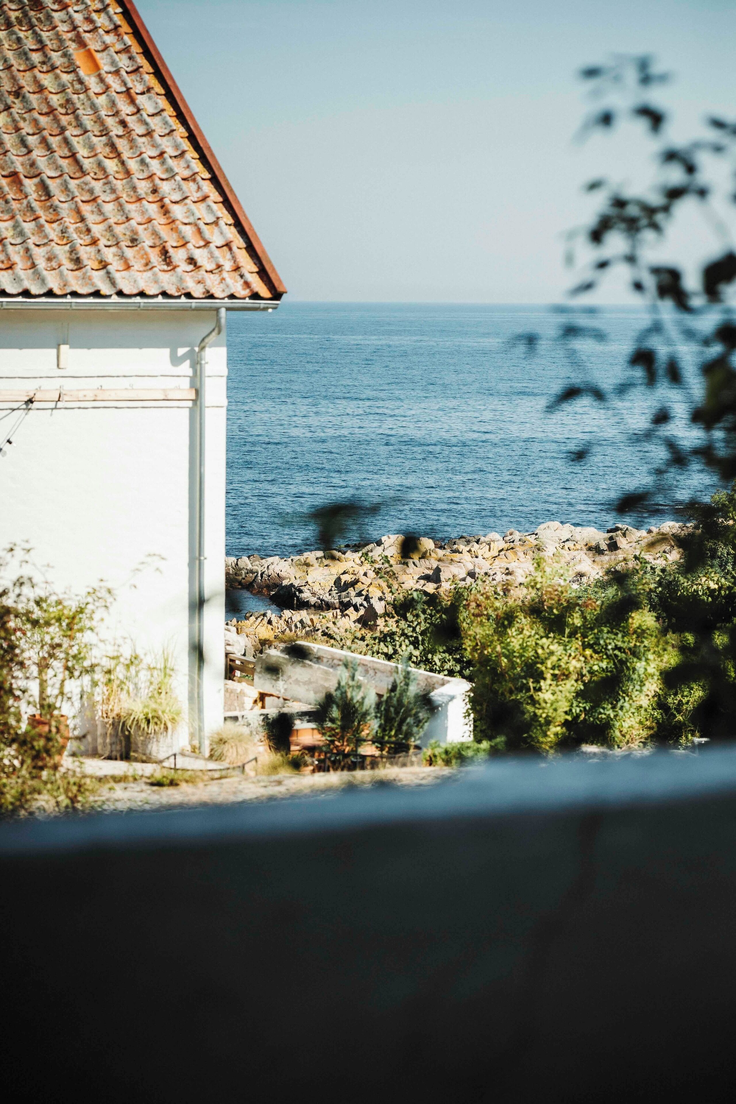 A coastal view with a white building, a tiled roof, and a rocky shoreline.