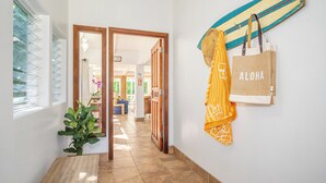 A hallway with a wooden door leading to a room, a surfboard, and a tote bag with "ALOHA" on the wall. - Private Hanalei house, close to the beach and town! TVNC 1298 (Hanalei)