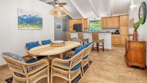 A dining area with wicker chairs and a table, a kitchen with wooden cabinets, and a ceiling fan. - Private Hanalei house, close to the beach and town! TVNC 1298 (Hanalei)