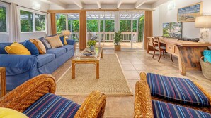 A spacious living area with a blue sofa, wicker chairs, a wooden desk, and a large window overlooking greenery. - Private Hanalei house, close to the beach and town! TVNC 1298 (Hanalei)
