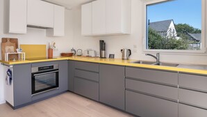 A modern kitchen with grey cabinets, a yellow countertop, and a window offering a view of a house and trees.