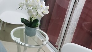 A balcony with a glass table, two white chairs, and a potted orchid.