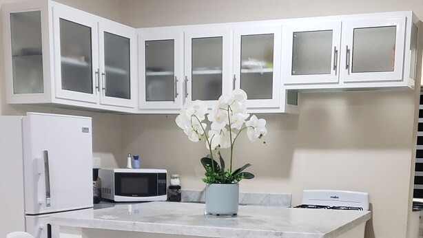 A modern kitchen with white cabinetry, a central island with two bar stools, a refrigerator, a microwave, and a gas stove.