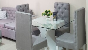 A modern living room with a glass-top coffee table, grey upholstered chairs, a grey sofa, and a mounted flat-screen TV.