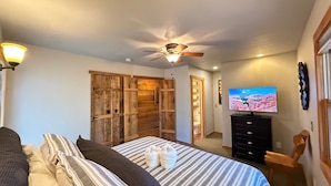Une chambre à coucher avec un lit, des oreillers, une télévision, un ventilateur de plafond et des murs en bois.