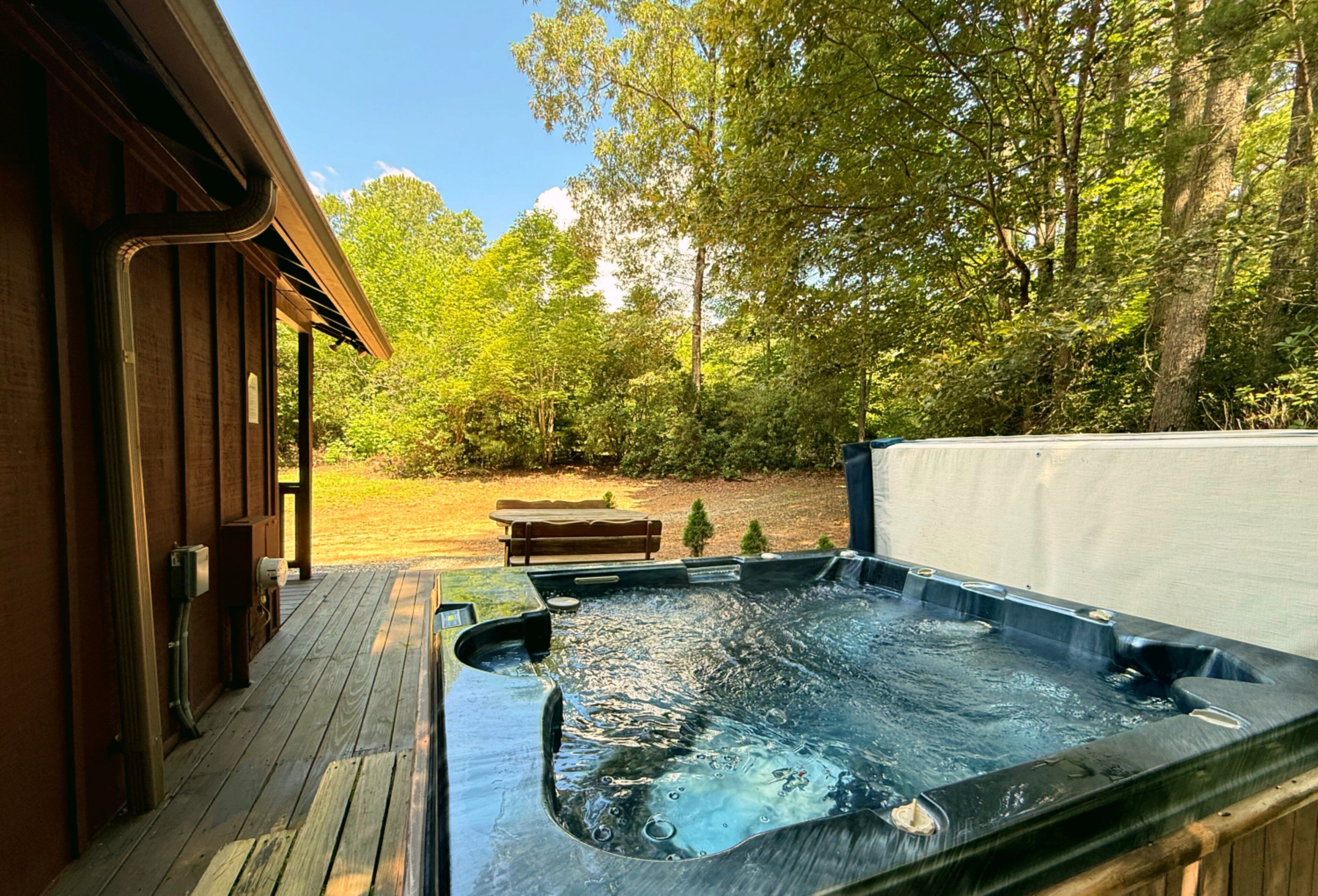 Ein Whirlpool mit einer Holzterrasse, einer Bank und bewaldeter Umgebung im Hintergrund.
