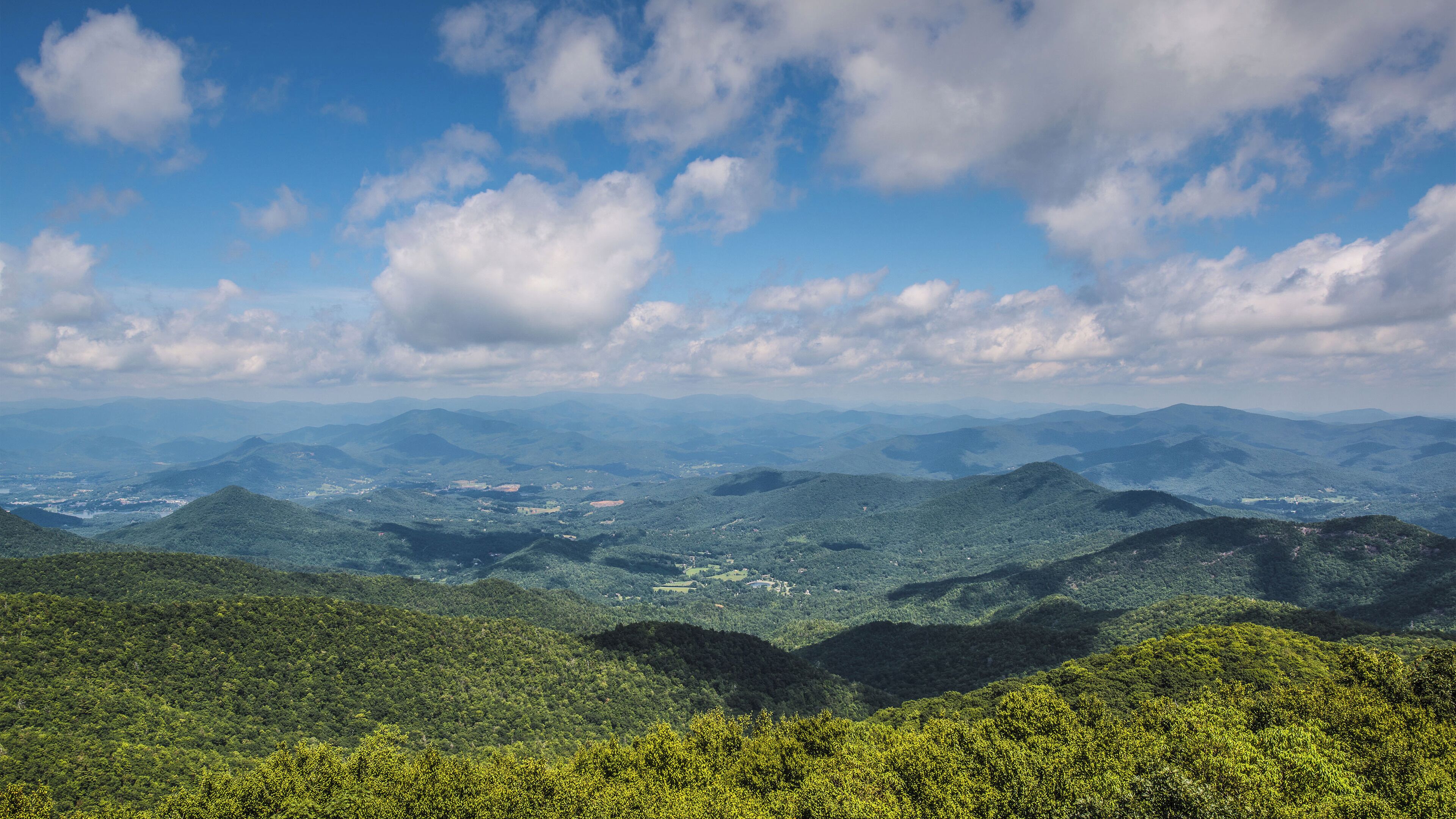 Ein weitreichender Panoramablick auf eine gebirgige Landschaft mit dichten, grünen Wäldern und blauem Himmel.