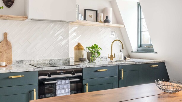 Una cucina moderna con zoccolo di piastrelle a spina di pesce, mobili scuri e piano di lavoro in legno.