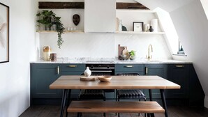 Una cucina moderna con mobili blu scuro, un tavolo da pranzo in legno e un piano di lavoro bianco.