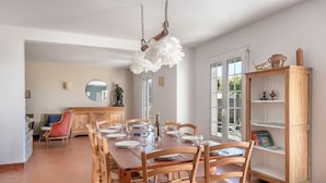 A dining area with a wooden table set for six, surrounded by wooden chairs. There is a wooden cabinet with shelves to the right, and a large window in the background. - Seafront house - 10 people - Garden (Saint-Gildas-de-Rhuys)