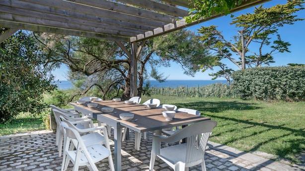 An outdoor dining area with a pergola, white plastic chairs, and a table set for four. - Seafront house - 10 people - Garden (Saint-Gildas-de-Rhuys)