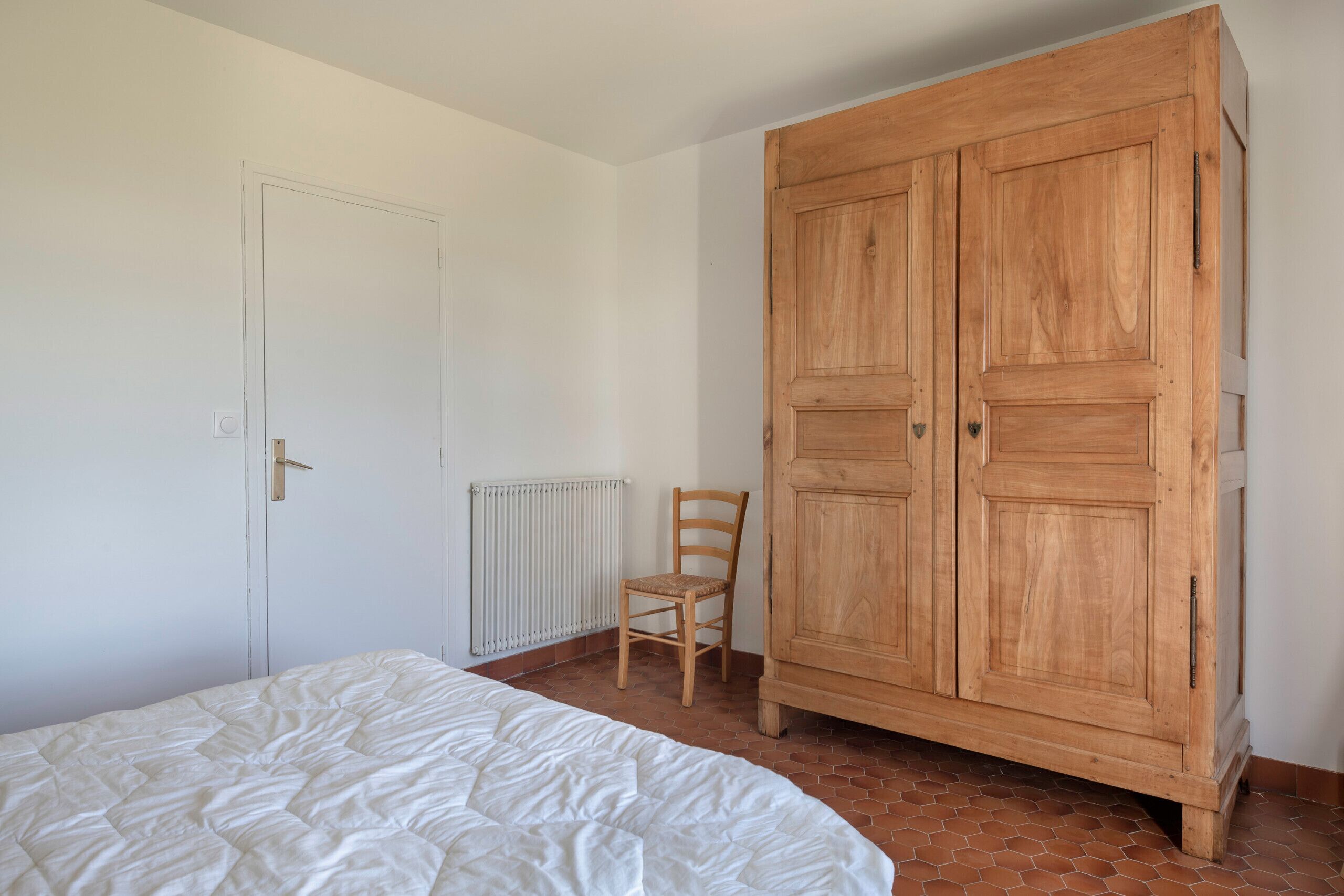 A bedroom with a bed, a wooden wardrobe, a radiator, and a chair.