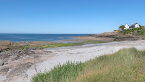 A coastal landscape with a rocky shoreline, a grassy foreground, and a white building with a sloped roof on a hill. - Seafront house - 10 people - Garden (Saint-Gildas-de-Rhuys)