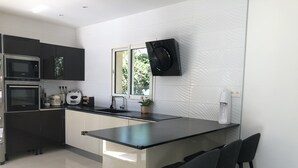 A modern kitchen with a central island, black bar stools, a built-in oven, a microwave, and a coffee machine. - Family home in Marseille (Marseille)