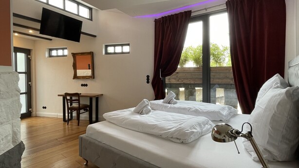 A hotel room with a bed, a desk, a chair, a TV, and a window with curtains. - Residenz im "alten Wasserturm" (Wuppertal)