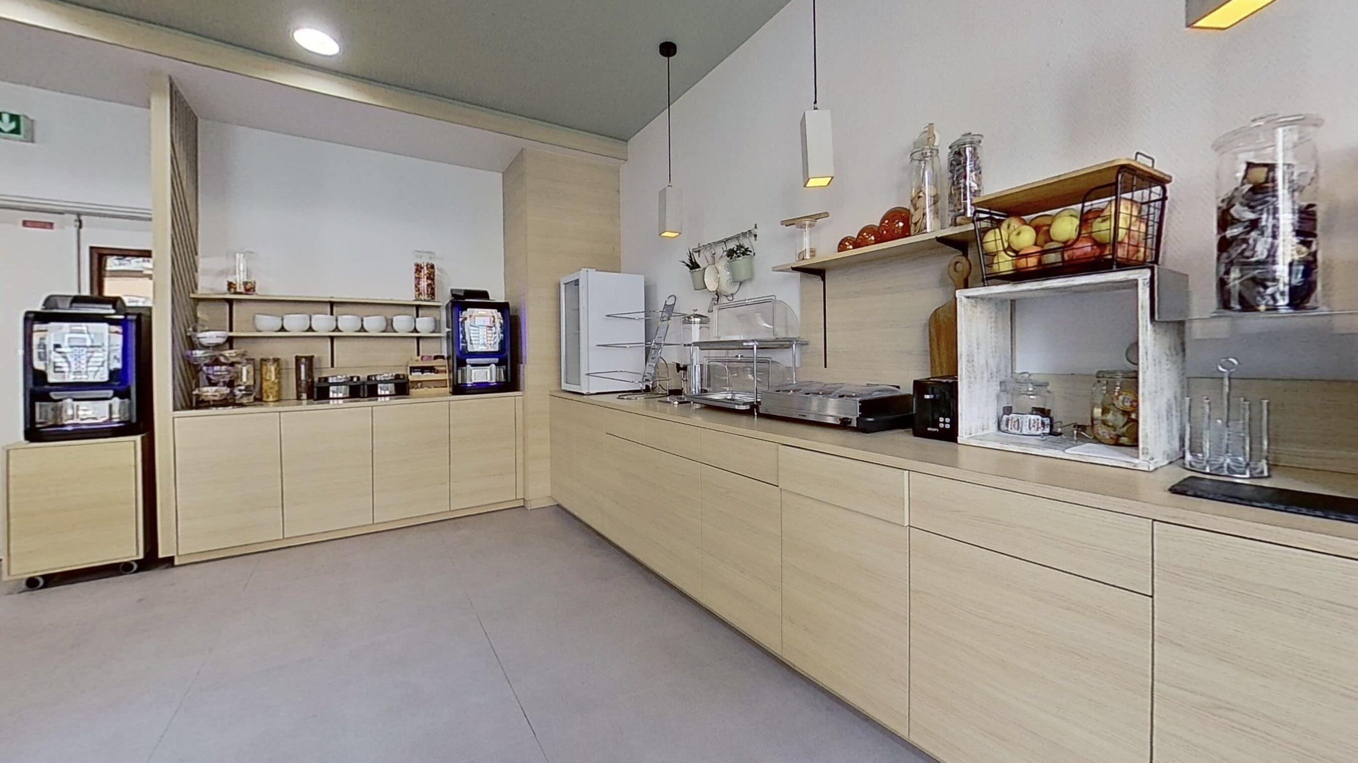 Une cuisine moderne dotée d’un long comptoir, équipée d’une machine à café, d’un four à micro-ondes et de diverses provisions rangées sur des étagères.