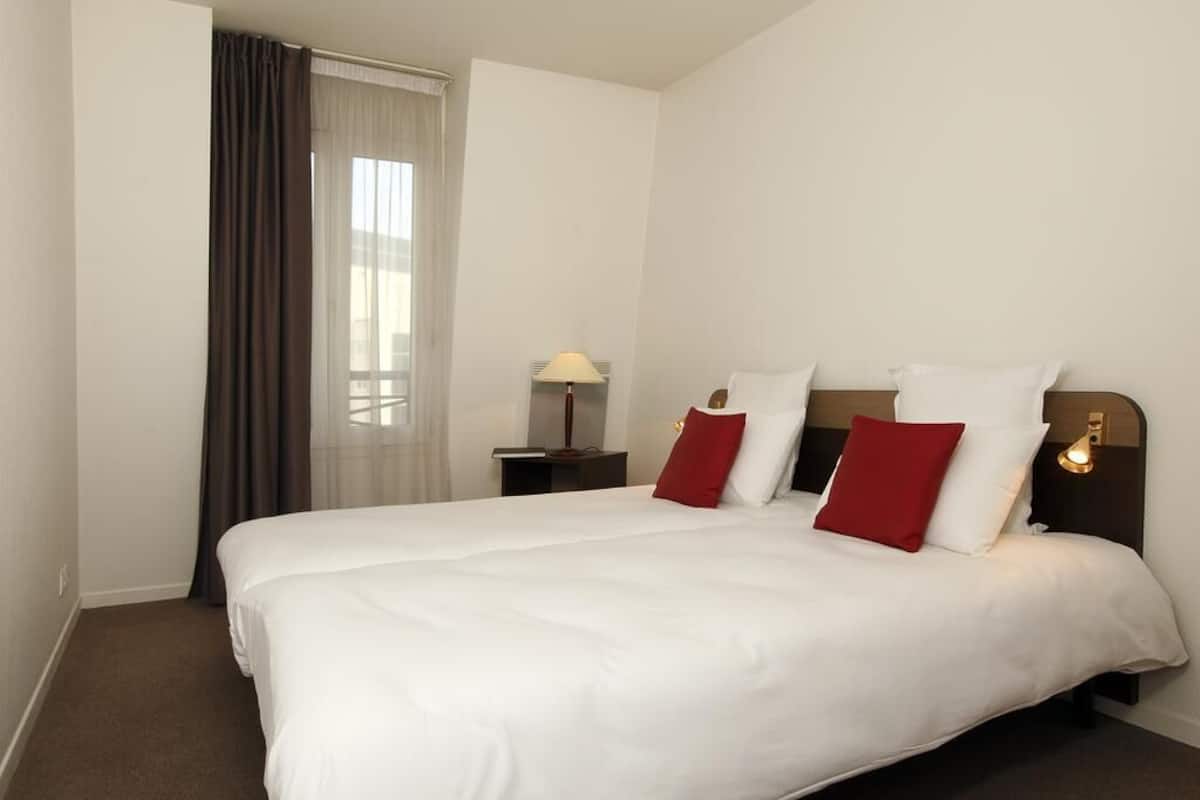 A hotel room with a large bed, a nightstand with a lamp, and a window with curtains.