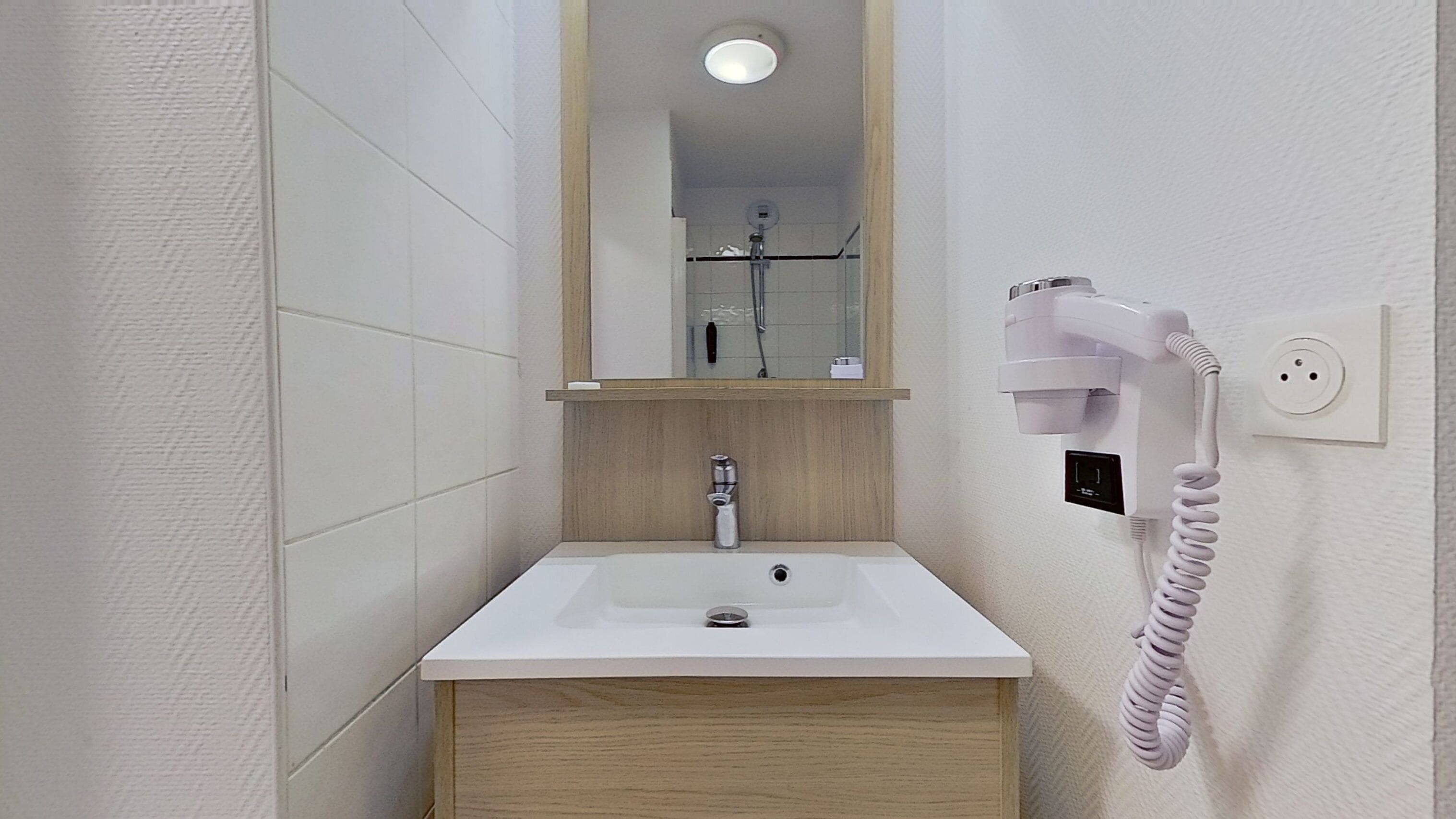 Un baño con un lavamanos blanco, tocador de madera y un secador de pelo montado en la pared.