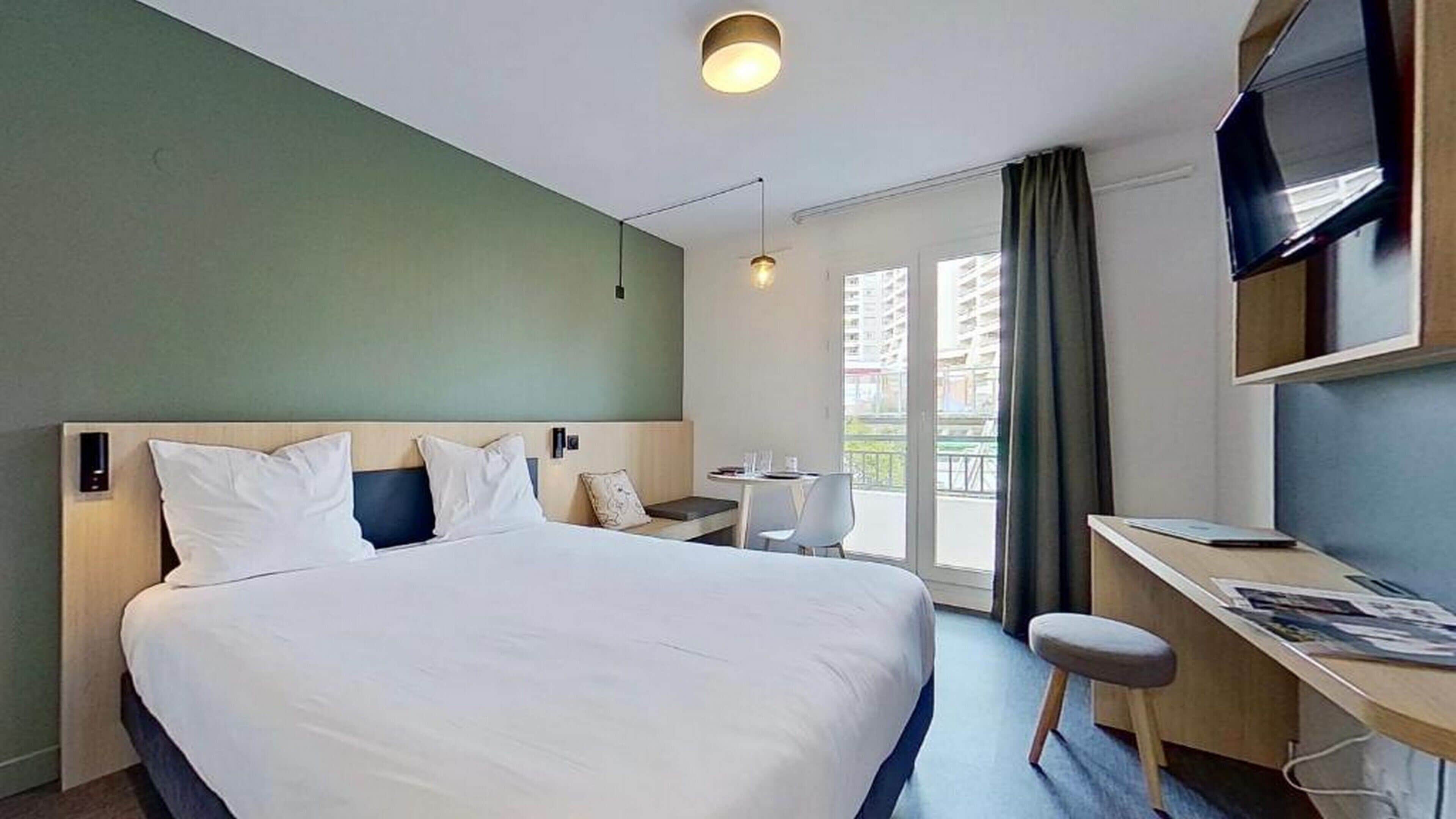 Une chambre d’hôtel avec un grand lit, un bureau, une chaise, une télévision et une fenêtre avec des rideaux.