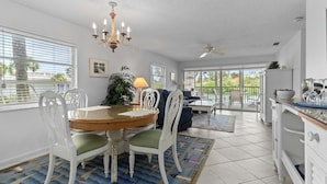 Un espace repas avec une table ronde, des chaises blanches, un lustre et une vue dégagée grâce à de grandes fenêtres.