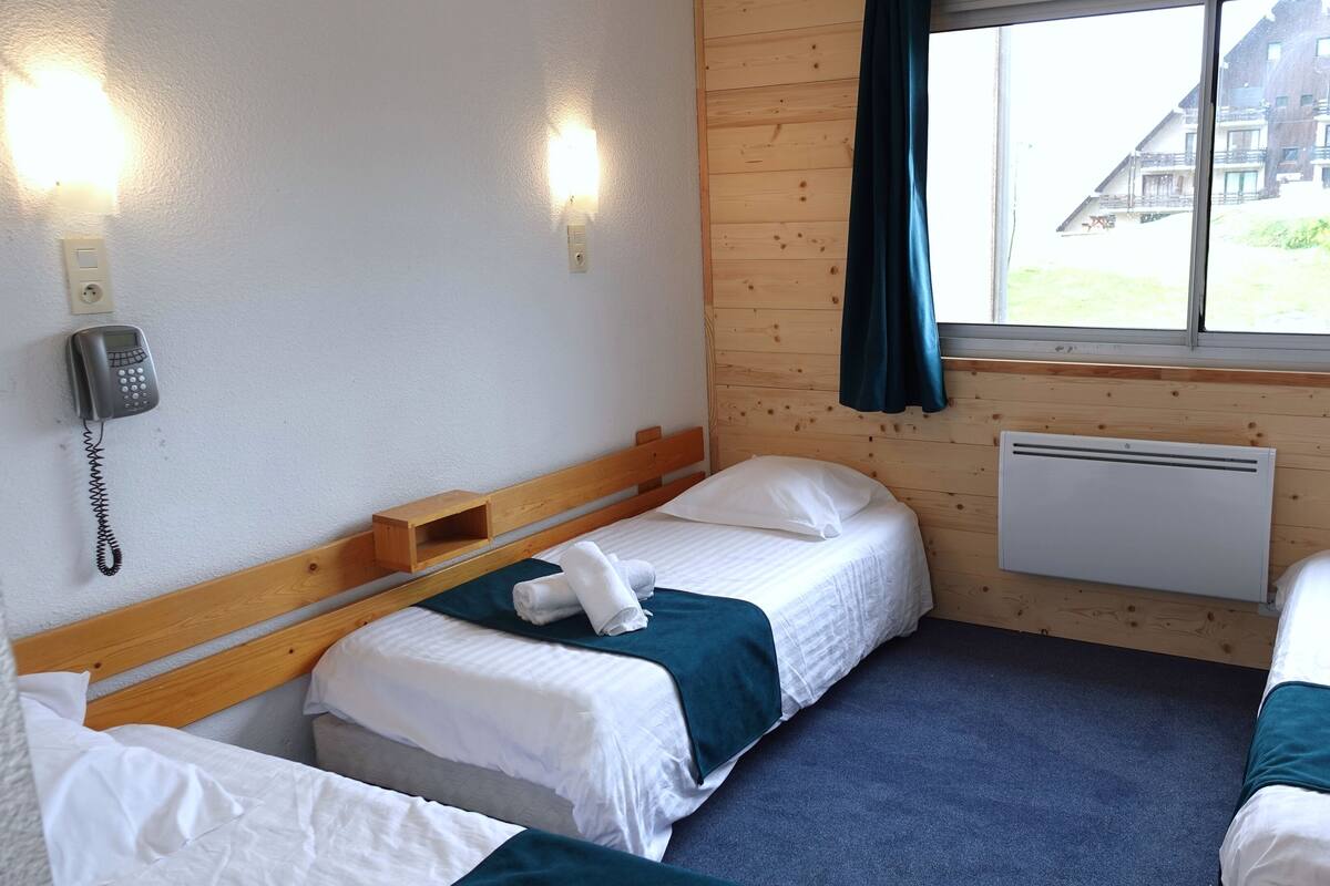 Ein Hotelzimmer mit zwei Betten, einem Telefon, einem Fenster mit Vorhängen und Blick auf ein Gebäude.