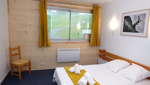 A hotel room with a bed, a chair, a window with curtains, a radiator, and a framed picture on the wall. - Le Balcon Des Ecrins (Reallon)