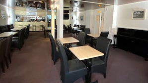 A restaurant with multiple tables and booths, a bar area, and a piano. - Le Balcon Des Ecrins (Reallon)
