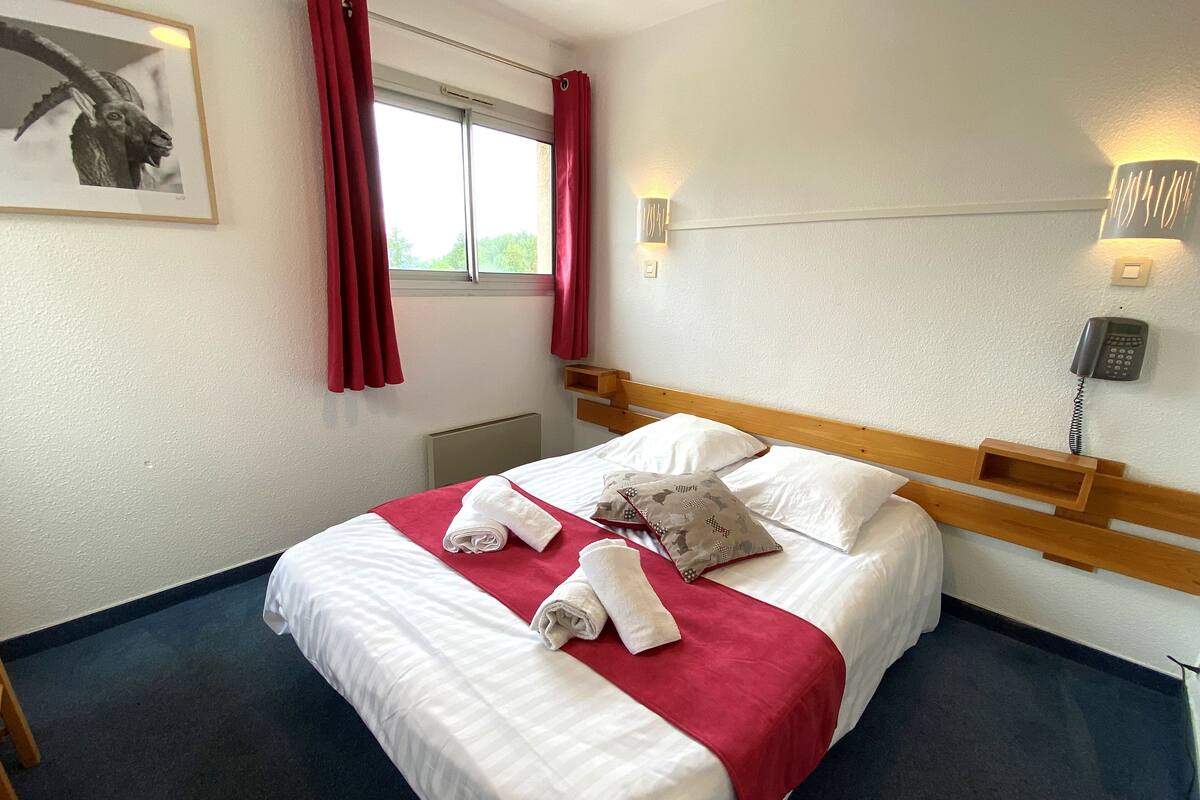 Ein Hotelzimmer mit einem Bett, roten Vorhängen, einem an der Wand montierten Telefon und einem gerahmten Bild.