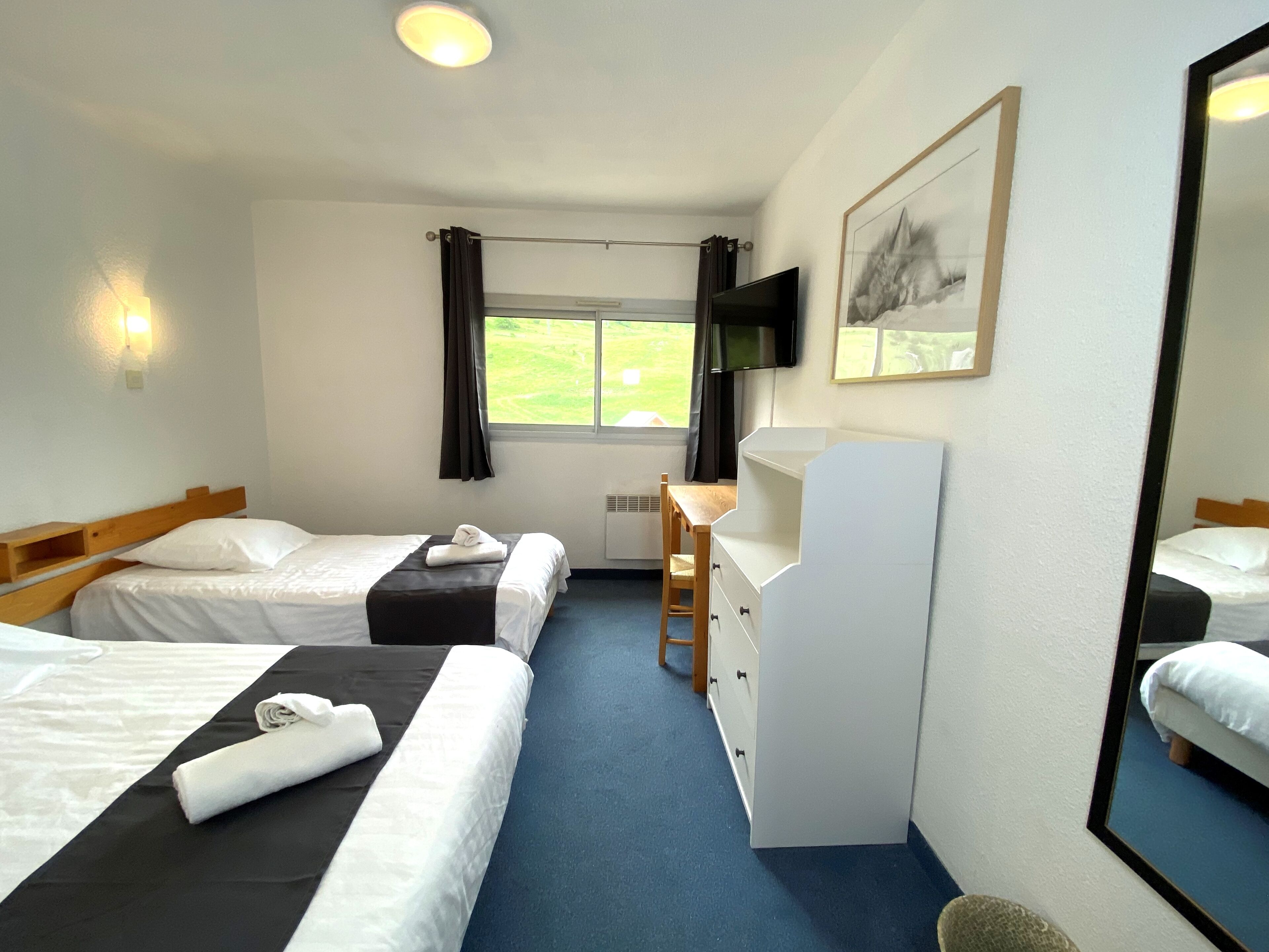 A hotel room with two beds, a desk, a chair, a TV, and a window with curtains.