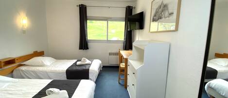 A hotel room with two beds, a desk, a chair, a TV, and a window with curtains.