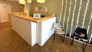 A reception area with a wooden counter, three pendant lights, a framed sign, a mirror, birch tree decor, and two chairs. - Le Balcon Des Ecrins (Reallon)