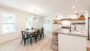 Una cucina moderna con mobili bianchi, un tavolo da pranzo in legno e sgabelli da bar.