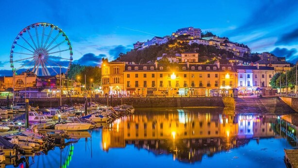 Un paysage urbain le long du littoral, avec une grande roue bien visible et un ensemble de bâtiments situés sur une colline.