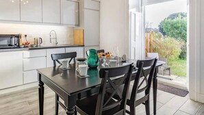 Une cuisine moderne avec des meubles blancs, une table à manger avec des chaises et une vue sur le jardin grâce à une grande fenêtre.
