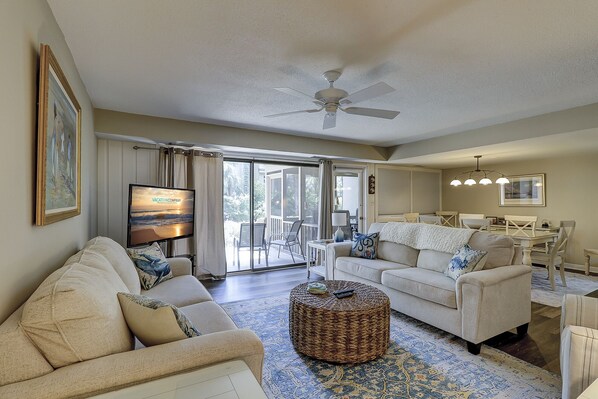 A spacious living room with a large flat-screen TV, a ceiling fan, and a dining area with a table and chairs.
