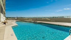 Une piscine aux eaux d’un bleu limpide, avec un escalier en métal, une terrasse en béton et un petit muret surmonté d’une rambarde.