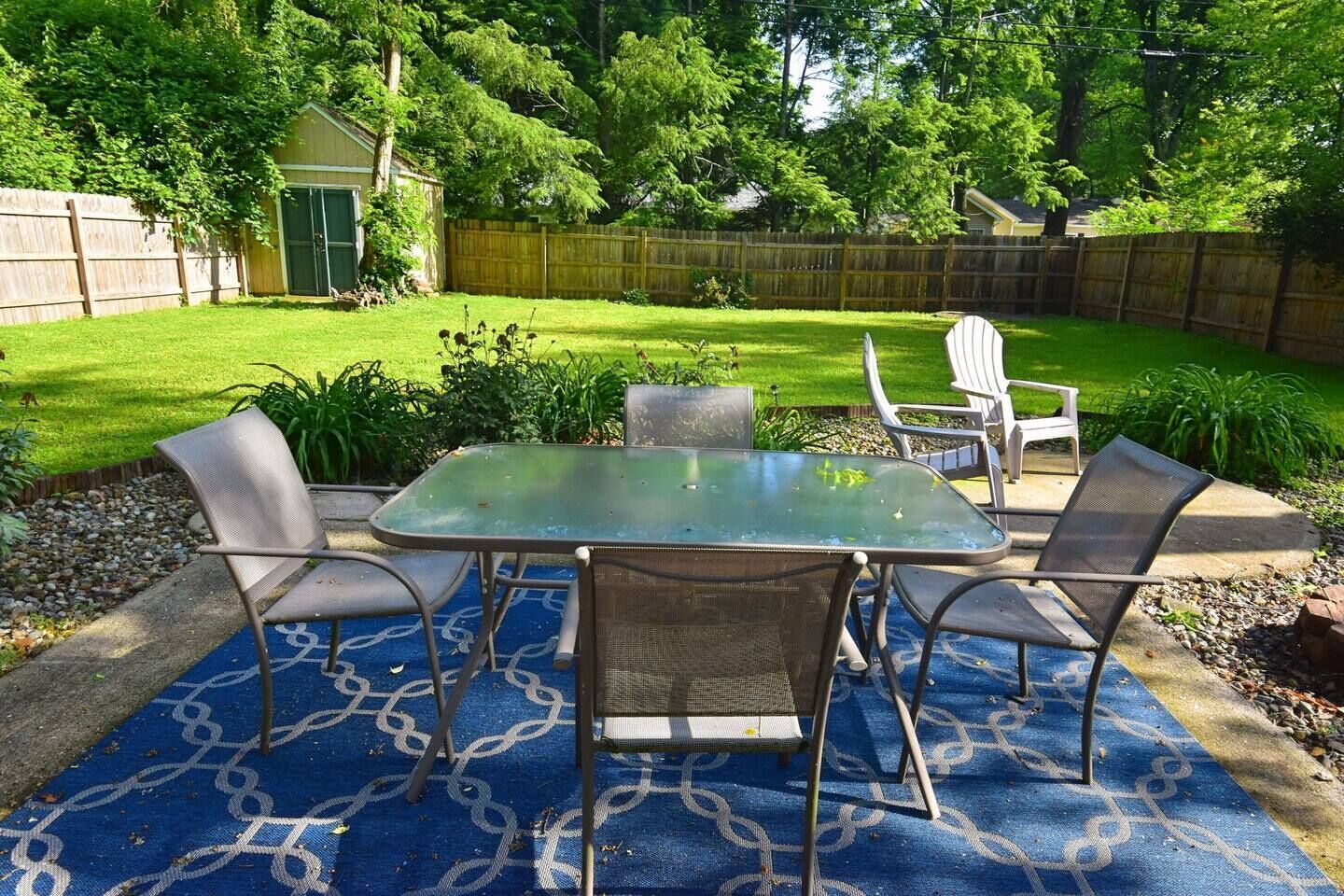 An outdoor patio with a glass-top table and four chairs, surrounded by a blue patterned rug.