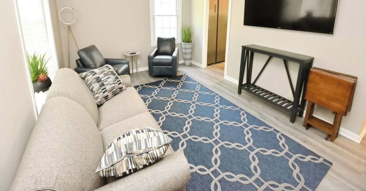 A living room with a sofa, a patterned rug, a TV, a small table, and a chair.